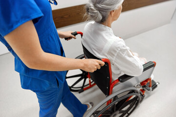 Poster - medicine, health and care concept - nurse taking senior woman patient in wheelchair at hospital corridor or nursing home