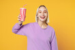 © ViDi Studio - Young blonde smiling caucasian woman 20s bob haircut bright makeup in casual basic purple shirt hold in plastic cup of soda cola bar with raised hand isolated on yellow background studio portrait