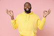 © ViDi Studio - Smiling young african american man 20s in casual yellow streetwear hoodie hold hands in yoga gesture relaxing meditating trying to calm down isolated on pastel pink color background studio portrait.