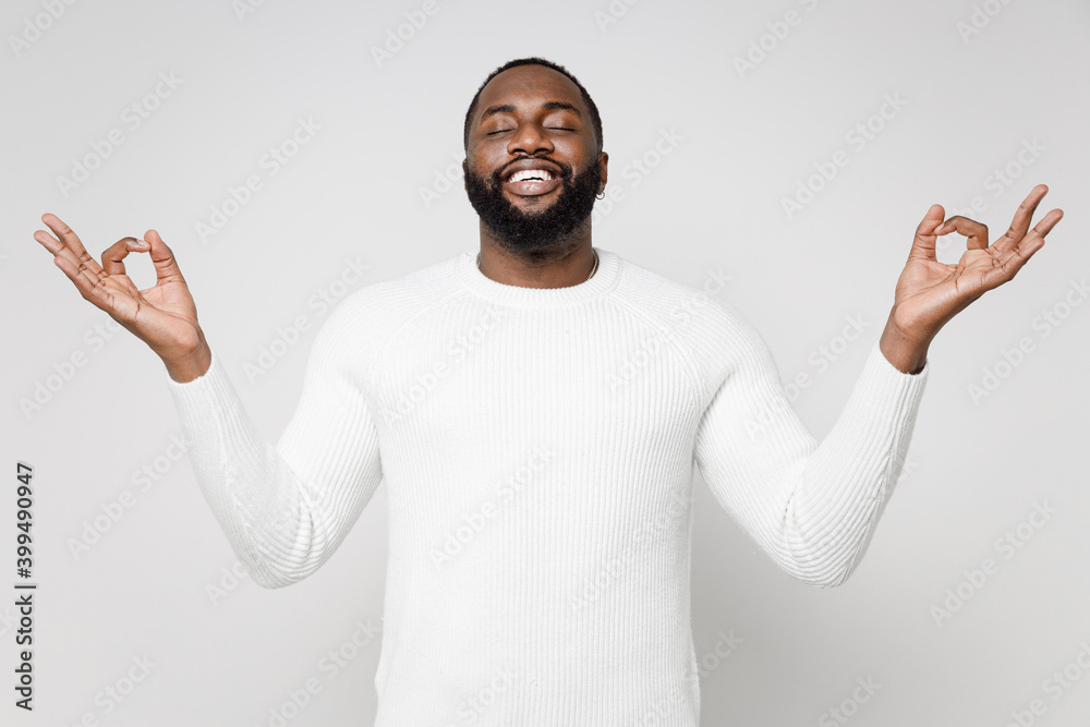 Smiling young african american man 20s wearing casual basic sweater standing hold hands in yoga gesture relaxing meditating trying to calm down isolated on white color wall background studio portrait. - obrazy, fototapety, plakaty 