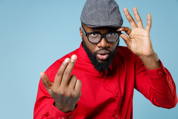 Wall Mural - Young bearded african american man 20s wearing casual red shirt cap eyeglasses standing calling with fingers gesture like says come to me isolated on pastel blue color wall background studio portrait.