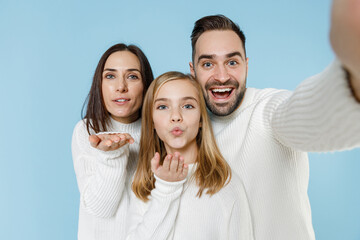 Wall Mural - Close up of pretty young parents mom dad child kid daughter teen girl in sweaters doing selfie shot on mobile phone blowing sending air kiss isolated on blue background. Family day parenthood concept.