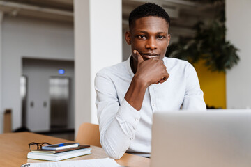 Poster - Afro american pleased man working with laptop while sitting in office