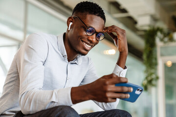 Poster - Afro american man in eyeglasses holding cellphone while sitting indoor