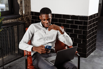 Poster - Afro american young man using laptop and smartphone while sitting