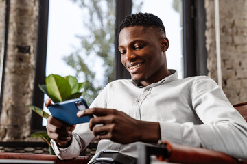 Poster - Afro american young man smiling and holding smartphone in armchair