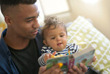 Fototapeta  - young african-american man reading book story to baby girl