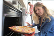 Young woman taking pizza out of the oven