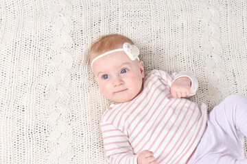 Cutest little 4- 5 months old caucasian baby girl with bow-heart in striped T-shirt on white plaid. Valentine day concept. Look at camera.