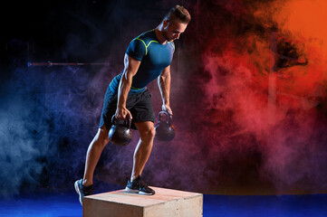 Poster - Attractive sportsman with kettle bell exercise in the fitness gym on the color smoke background. Copyspace area for advertise slogan or text message. Functional training and crossfit concept.