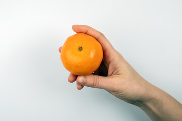 Wall Mural - One tangerine in a woman's hand on a white background