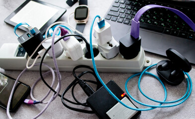 Many gadgets: smartphone, wireless headphones, laptop, smart watch, camera battery and e-book are charging on one power strip