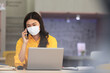 © 220 Selfmade studio - New normal of Asian woman in yellow shirt wearing surgical face mask talking with customer work laptop to get ideas and requirement in Business startup at modern office or Co-working space
