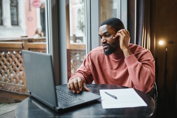 Afro american talks video chat on computer sits in cafe with cup of coffee. Black man calls on laptop on video link and speaks. He wears in shirt and suit jacket. Video link online connection.