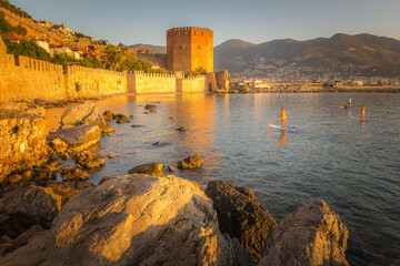 SUP surfers row on their boards early in the morning in the port of Alanya near a quiet beach under the walls of an ancient medieval fortress.