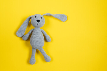 grey knitted toy rabbit on yellow background with copy space. top view