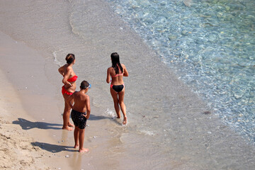 People having fun on a sea beach, top view. Woman in swimsuit and teens on a sand, family holiday and vacation