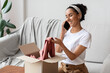 Happy young woman opening carton box and talking on phone