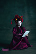 Scrolling tablet. Young japanese woman as geisha isolated on dark green background. Retro style, comparison of eras concept. Beautiful female model like bright historical character, old-fashioned.