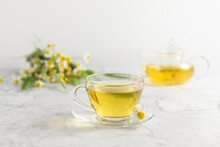Glass Cups And Teapot With Chamomile Tea On A White Background. A Bouquet Of Daisies.