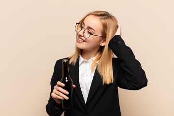 Wall Mural - young blonde woman smiling cheerfully and casually, taking hand to head with a positive, happy and confident look