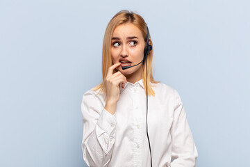 Wall Mural - young blonde woman with surprised, nervous, worried or frightened look, looking to the side towards copy space