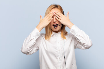 Wall Mural - young blonde woman smiling and feeling happy, covering eyes with both hands and waiting for unbelievable surprise