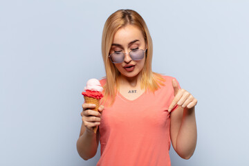 Wall Mural - young blonde woman with open mouth pointing downwards with both hands, looking shocked, amazed and surprised