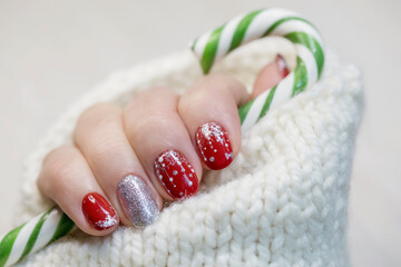 A female hand with a red New Year's manicure holds a candy cane.