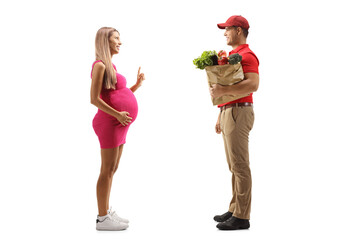 Canvas Print - Full length profile shot of a pregnant woman in a pink dress talking to a delivery guy with a grocery bag