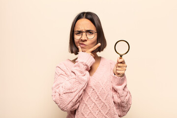 Canvas Print - young hispanic woman looking serious, thoughtful and distrustful, with one arm crossed and hand on chin, weighting options