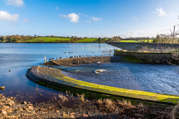 Sticker - A view across the overflow bank along the barrage of Thornton Reservoir, UK on a bright sunny day