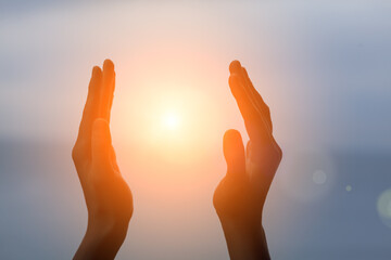 young woman raising hands praying at sunset or sunrise light