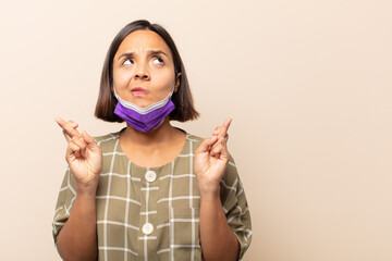 Wall Mural - young hispanic woman crossing fingers anxiously and hoping for good luck with a worried look