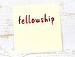Yellow sticky note on wooden wall with handwritten word fellowship