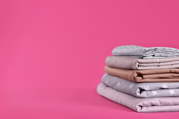 Stack of clean bed sheets on pink background. Space for text