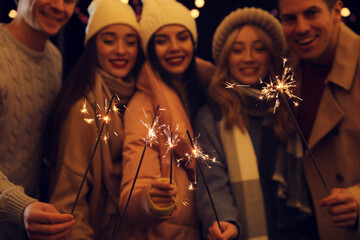 Wall Mural - Group of people holding burning sparklers, focus on fireworks