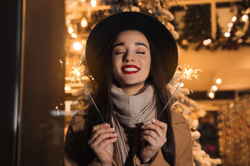 Wall Mural - Woman in warm clothes holding burning sparklers on blurred background