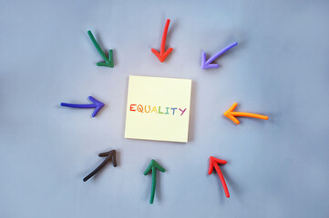 Top view of equality word on yellow sticky note with colorful arrow on grey background. Social issue concept and lgbt idea