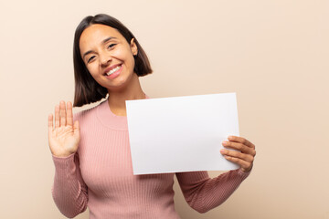 Canvas Print - young latin woman smiling happily and cheerfully, waving hand, welcoming and greeting you, or saying goodbye