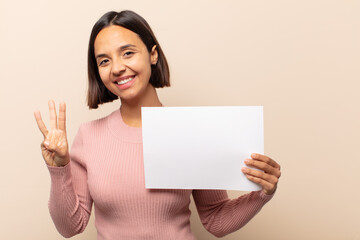 Canvas Print - young latin woman smiling and looking friendly, showing number three or third with hand forward, counting down