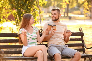 Sticker - Young couple eating sweet donuts and drinking coffee outdoors