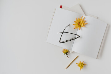 Wall Mural - Minimalist home office desk workspace. Blank paper sheet notebook, glasses, yellow flower bud, stationery. Flat lay, top view. Copy space mockup template for blog, social media, website.