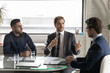 © fizkes - Motivated diverse multiracial businessmen gather at meeting in boardroom talk discuss idea together. Confident multiethnic businesspeople male partners brainstorm at office briefing. Teamwork concept.