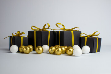 Festive background. Black gifts with a gold ribbon and gold christmas balls on white background. Set of Christmas gifts on a white background. A white teddy bear is sitting among the gift.