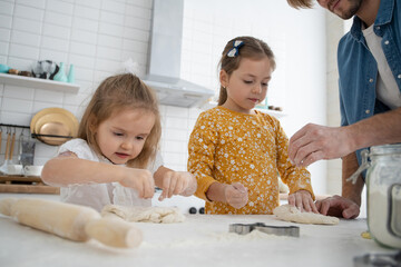 Wall Mural - smiling father and daughters baking in the kitchen and having fun