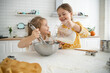 happy sisters children girls bake cookies, knead dough, play with flour and laugh in the kitchen.