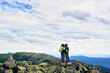 © anatoliy_gleb - Rear view young people are standing in embrace on stones at peak with beautiful view valley Carpathian mountains. Girl and guy wearing jackets under cloudy sky on windy day. Active lifestyle