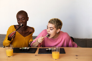 Two happy beautiful women sitting while eating vegan sushi rolls