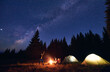 © anatoliy_gleb - Man showing his friends Milky Way over tent city. Guys are sitting by the campfire on the background of the spruce forest and enjoying the evening starry sky. Outdoor recreation, touristm concept